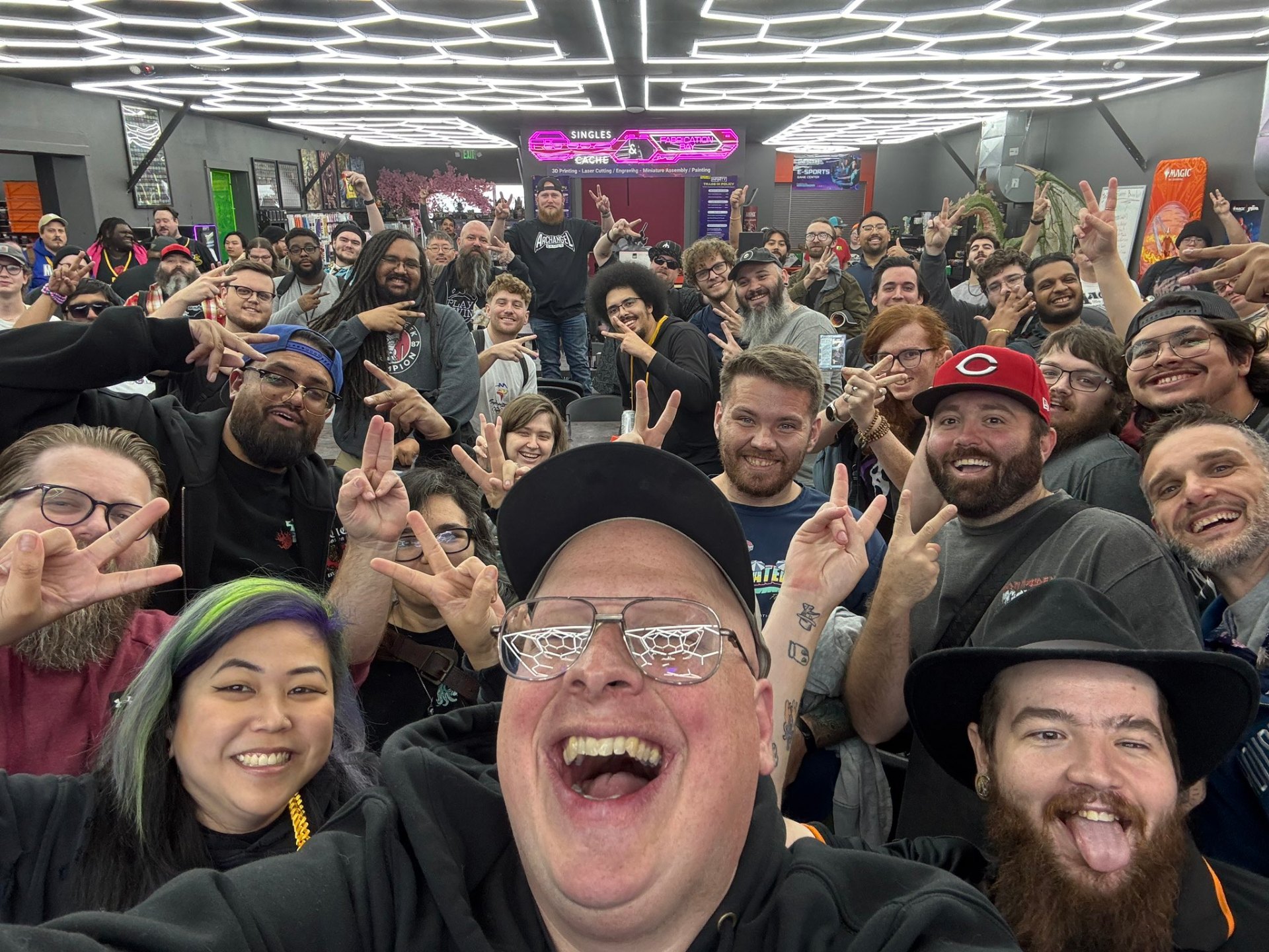 IGL2 store interior packed with the Clarksville MTG community during a Magic: The Gathering event, hex-lit ceiling and neon Singles & Fabrication Bay sign overhead.